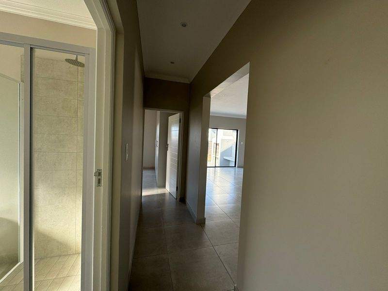 A bright, neutral hallway featuring tiled flooring and recessed lighting, providing access to a bathroom and open-plan living area.