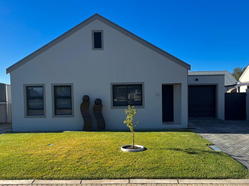 A well-maintained modern single-story house featuring a gabled roof, paved driveway, integrated garage, and a neat front lawn.