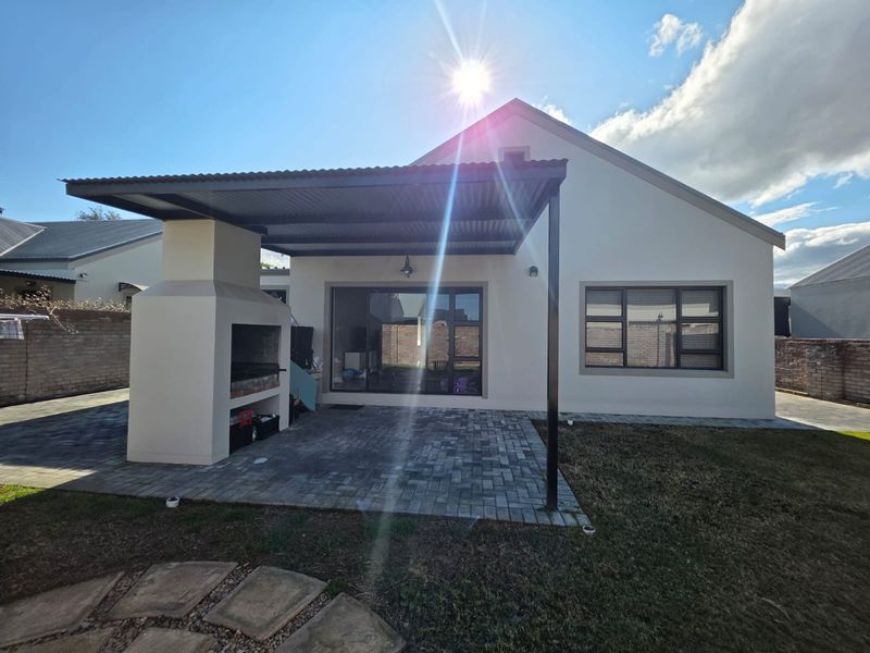 Rear view of the property featuring a paved patio area with a built-in braai and a covered roof structure.