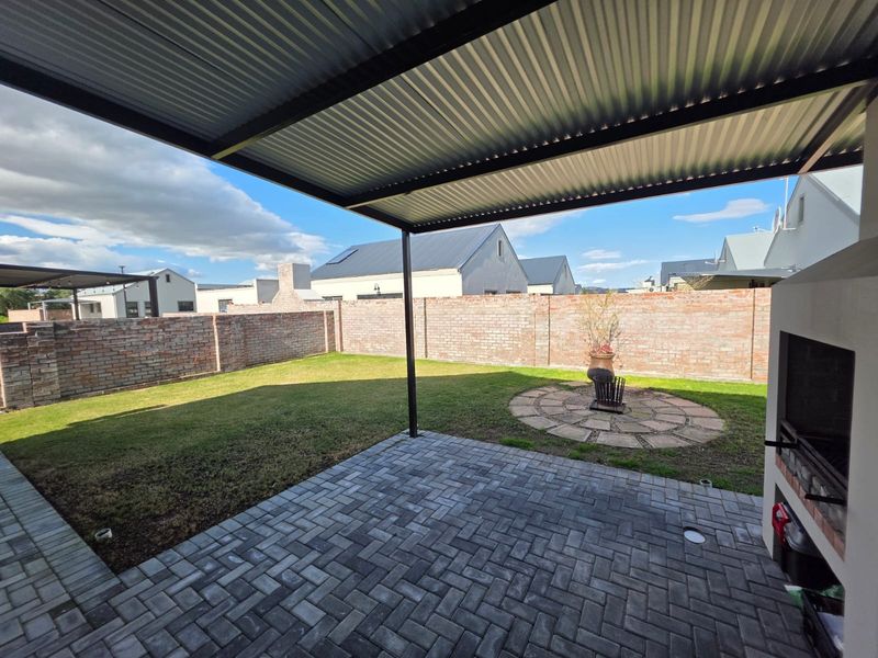 Covered patio area featuring a built-in braai, paved flooring, and a private garden with a brick boundary wall.