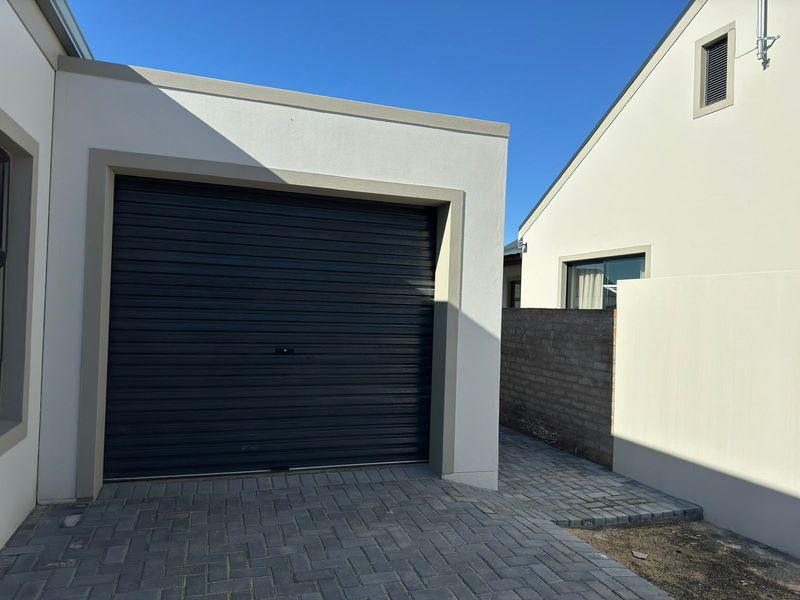 Modern garage exterior featuring a dark roller door, paved driveway, and clean white rendered walls in a contemporary residential setting.