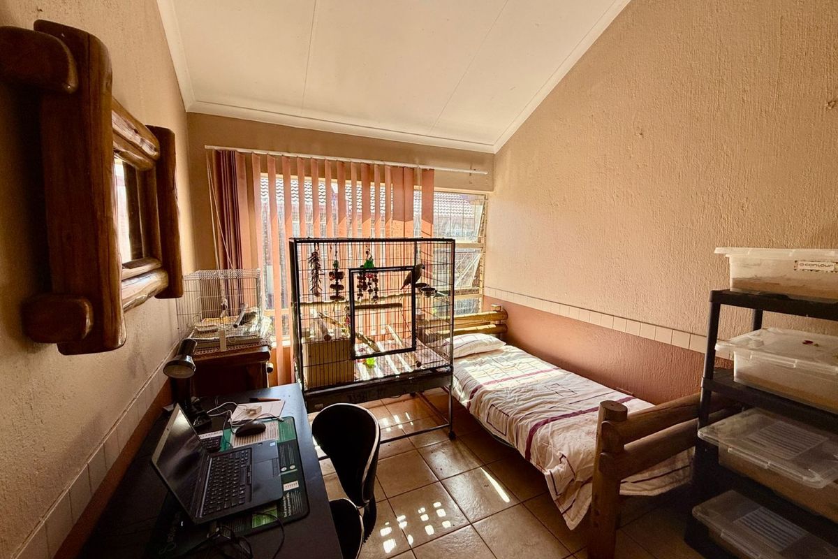 A bedroom featuring tiled flooring, a raked ceiling, and large windows with vertical blinds, providing a functional space with natural light.