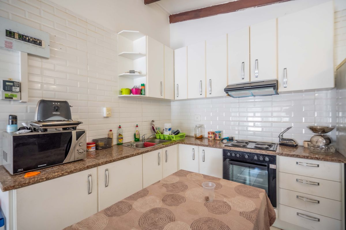 A functional kitchen featuring white cabinetry, granite countertops, a subway tile backsplash, and integrated cooking appliances including an oven and extractor fan.