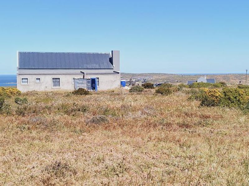 A view of a detached residential structure situated on a large, undeveloped coastal plot with natural vegetation.