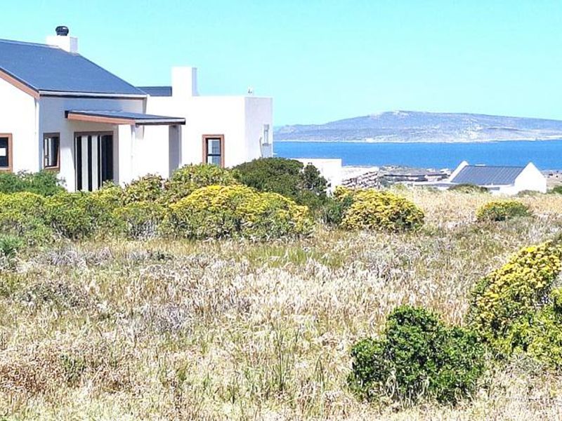 A view of the rear elevation of a residential property featuring a metal roof and plastered walls, set against a coastal landscape.