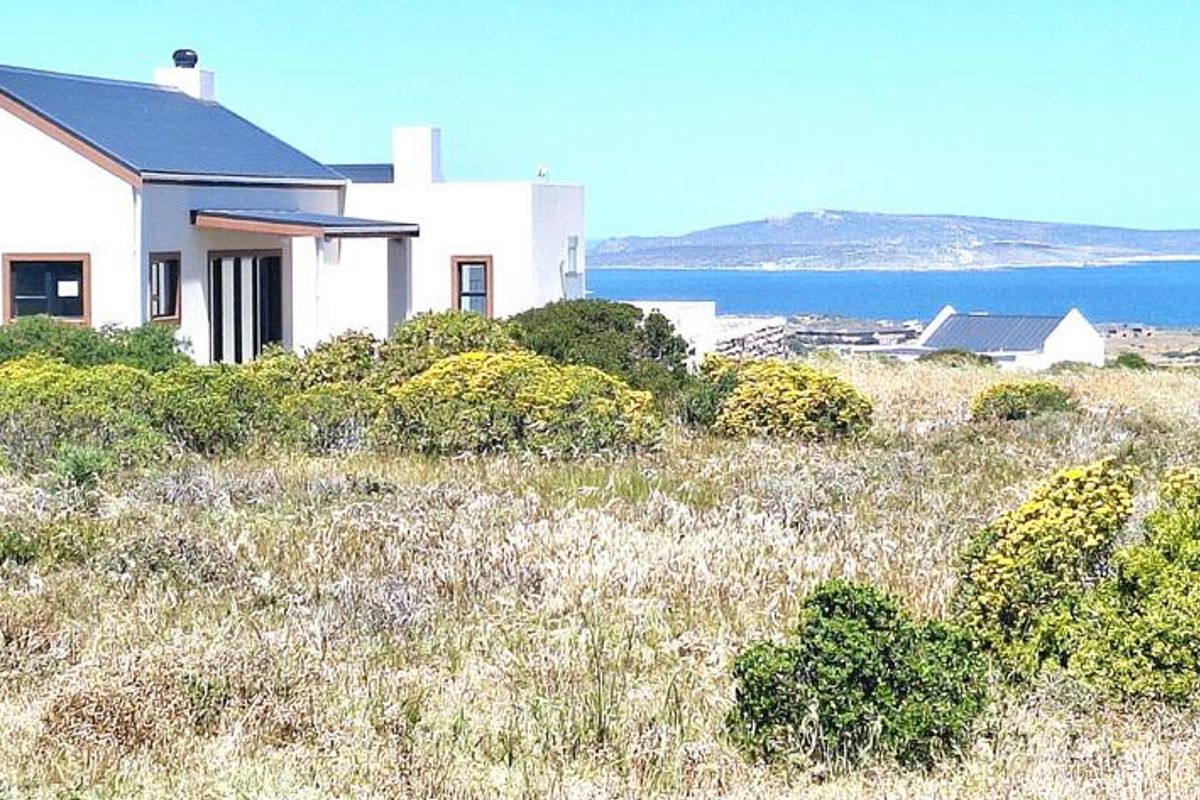 A view of the rear elevation of a residential property featuring a metal roof and plastered walls, set against a coastal landscape.