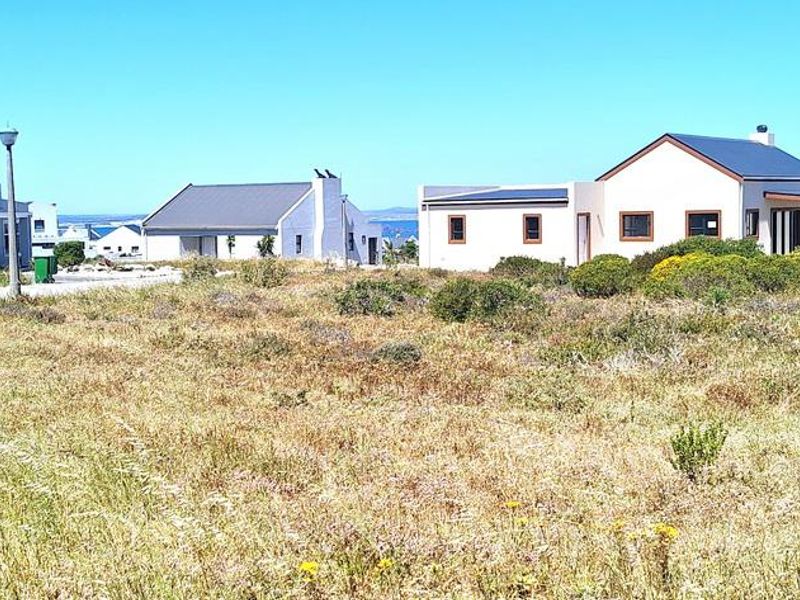 A view of a vacant residential plot in a developed coastal estate, featuring surrounding modern homes and established infrastructure.