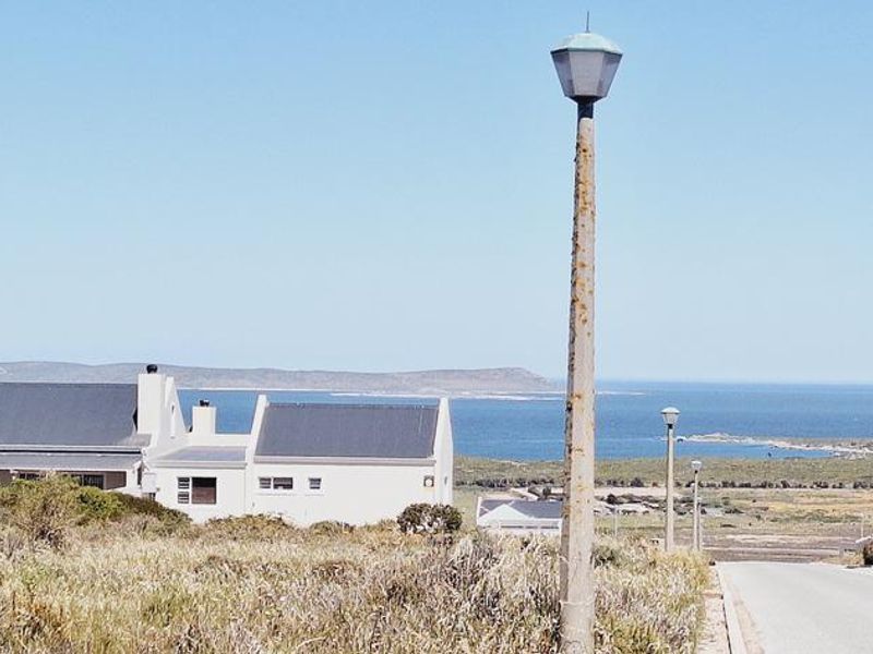A street view of a residential area featuring a paved road, street lighting, and scenic coastal views in the background.