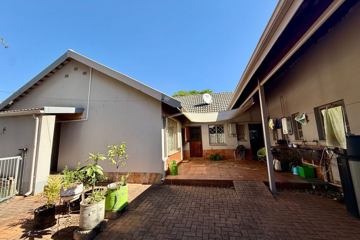 A rear courtyard area featuring paved flooring, a covered patio section, and direct access to the main house structure.