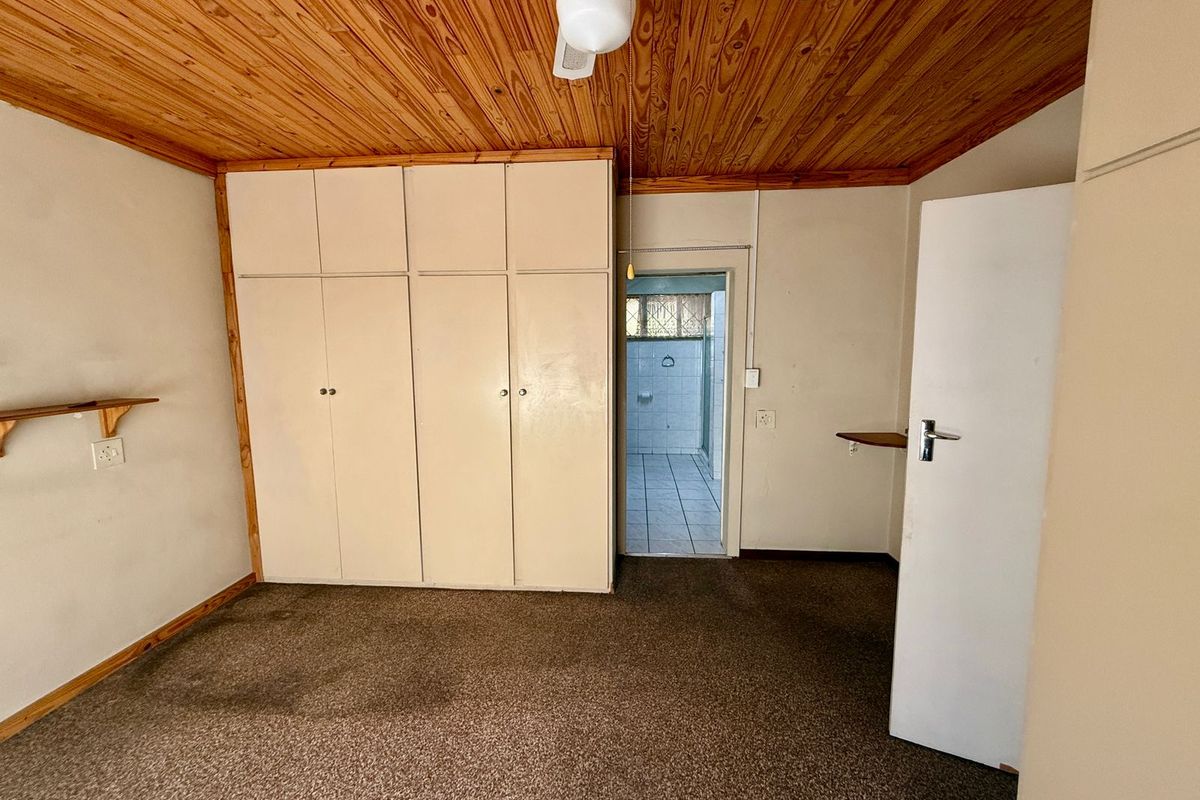 A bedroom featuring built-in cupboards, a wood-paneled ceiling, and an attached en-suite bathroom, offering a functional space ready for modernization.