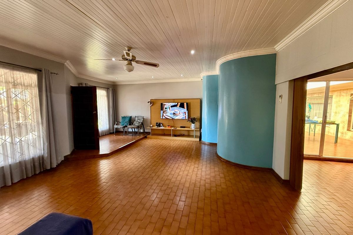 Spacious living room featuring a raised platform area, curved feature wall, tiled flooring, and a white tongue-and-groove ceiling with a central fan.