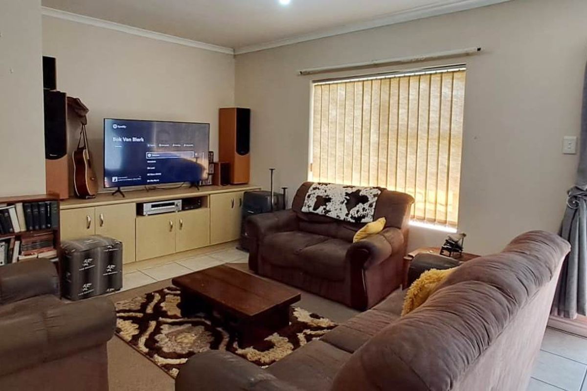 A comfortable living room featuring tiled flooring, built-in cabinetry, and a sliding glass door with security gate providing access to the exterior.