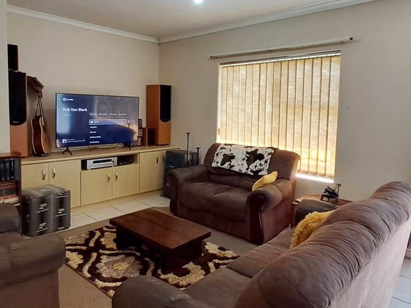 A comfortable living room featuring tiled flooring, built-in cabinetry, and a sliding glass door with security gate providing access to the exterior.