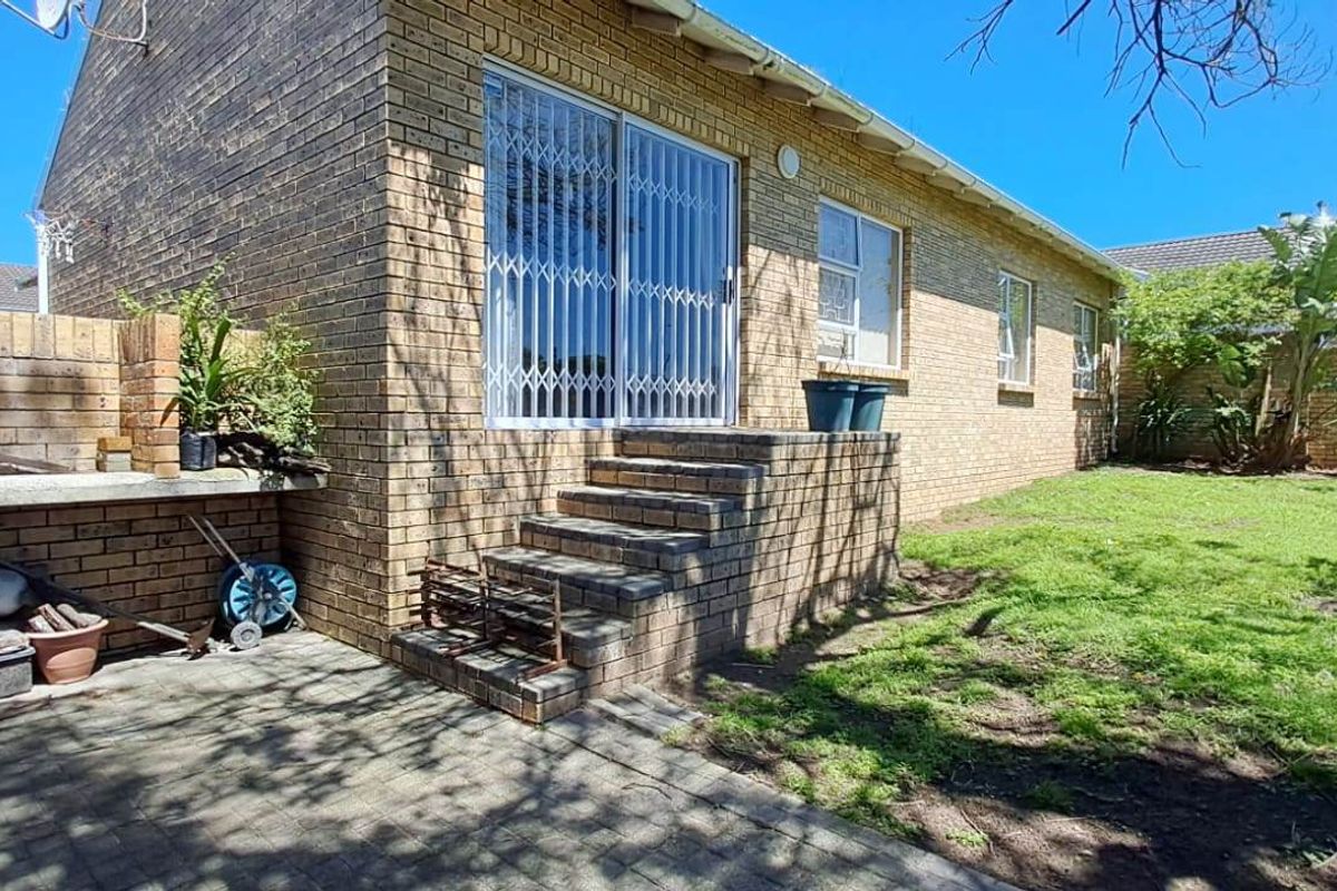 Rear exterior view of the townhouse featuring a brick facade, paved patio area with built-in brick counter, and a private garden space.