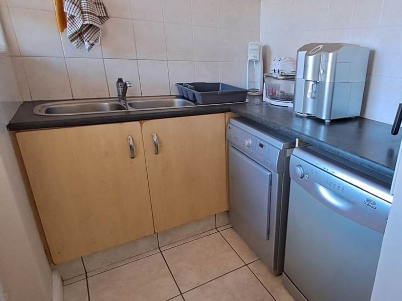 A functional laundry area featuring a double stainless steel sink, laminate cabinetry, tiled splashback, and space for under-counter appliances.