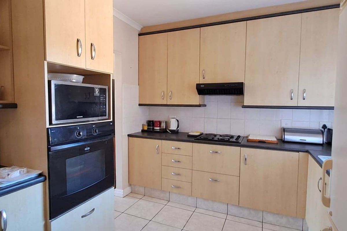 Functional kitchen featuring light wood-finish cabinetry, built-in oven and microwave, gas hob with extractor fan, and tiled flooring.