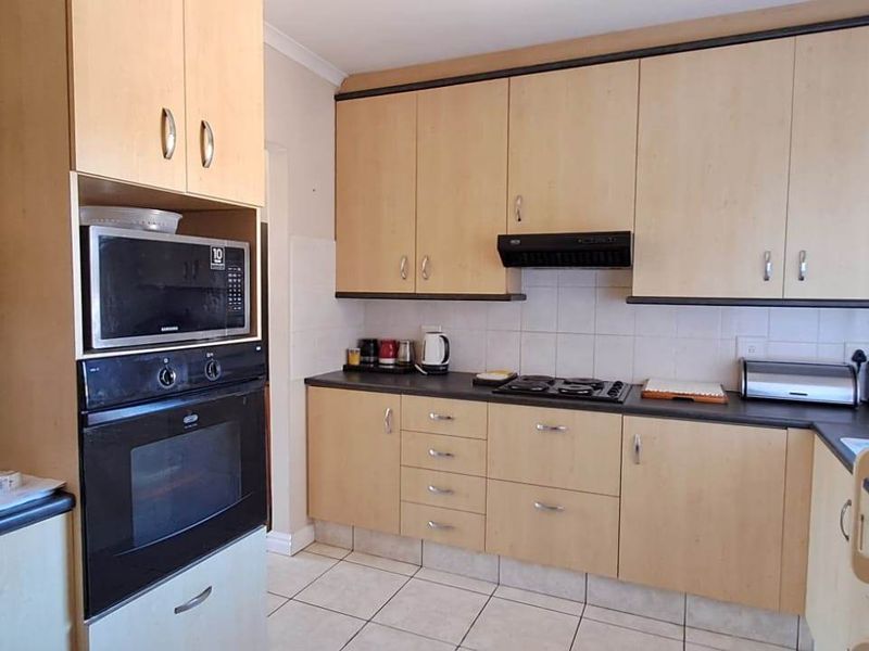 Functional kitchen featuring light wood-finish cabinetry, built-in oven and microwave, gas hob with extractor fan, and tiled flooring.