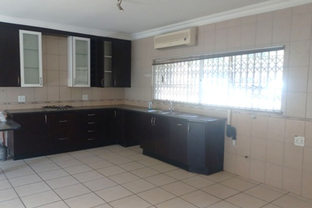 A functional kitchen featuring dark wood cabinetry, tiled splashbacks, a built-in hob, and a window with security bars.