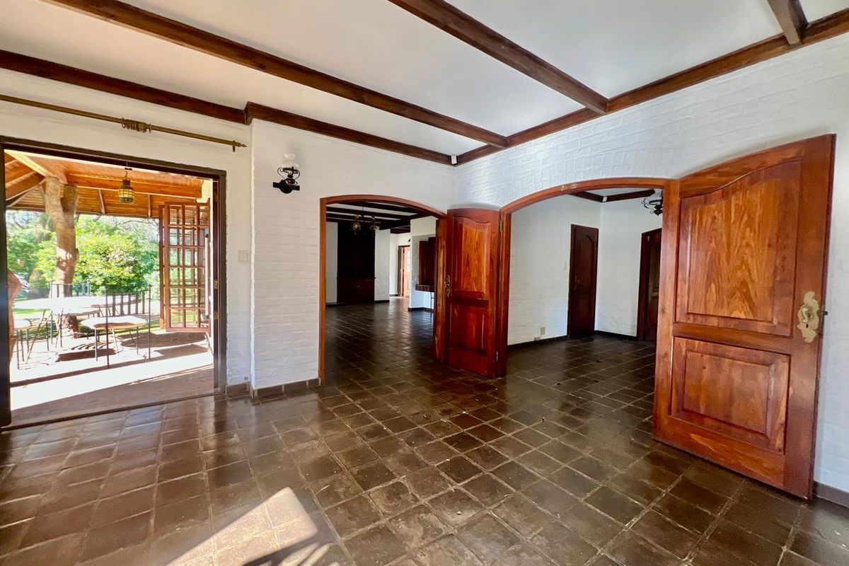 Spacious living area featuring exposed timber ceiling beams, terracotta floor tiles, and arched doorways leading to a covered patio and adjacent rooms.