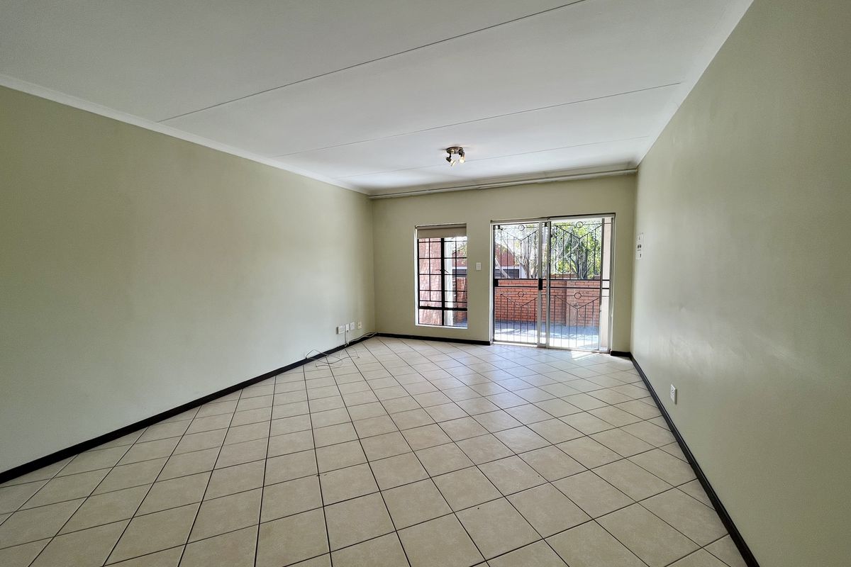 A bright, empty living room featuring neutral tiled flooring, coved ceilings, and a sliding glass door providing access to the exterior.