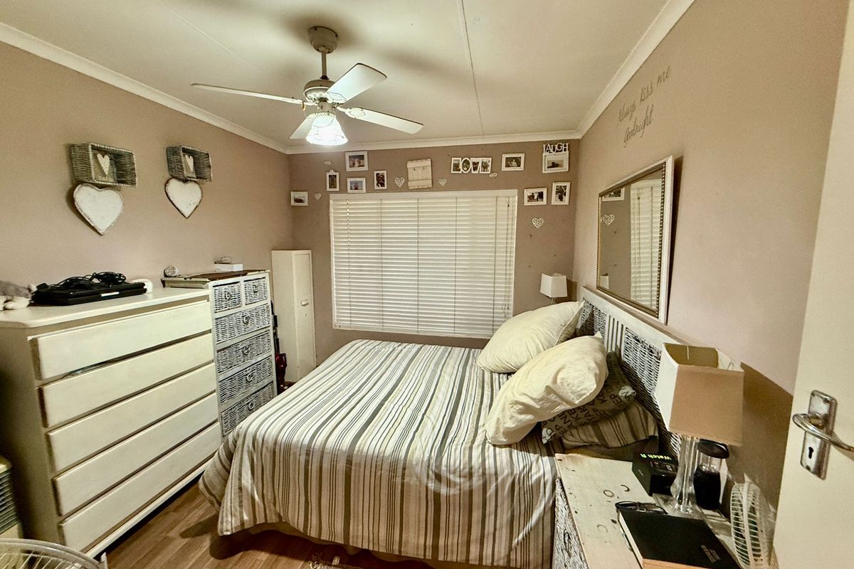 A cozy bedroom featuring a ceiling fan, horizontal window blinds, and laminate flooring, providing a comfortable and functional sleeping space.