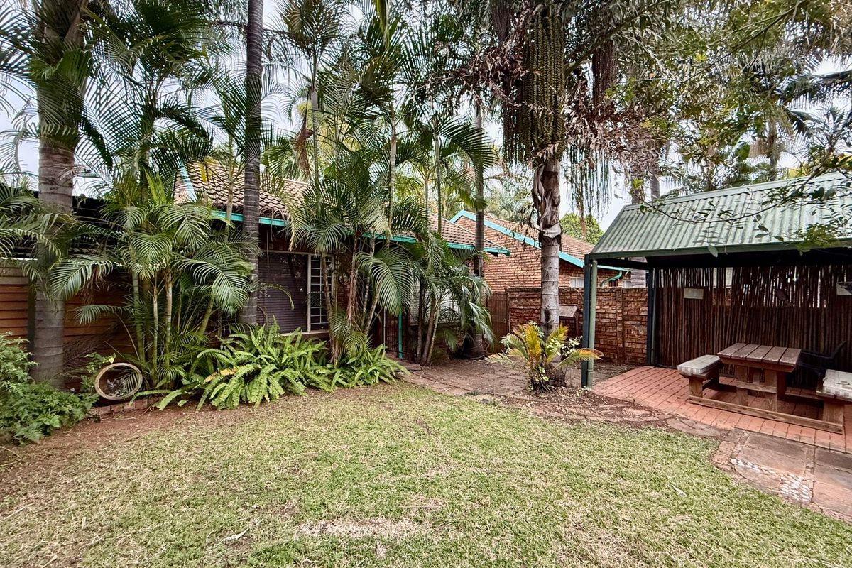 A private rear garden featuring a lawn, mature palm trees, and a covered patio area with a built-in structure.
