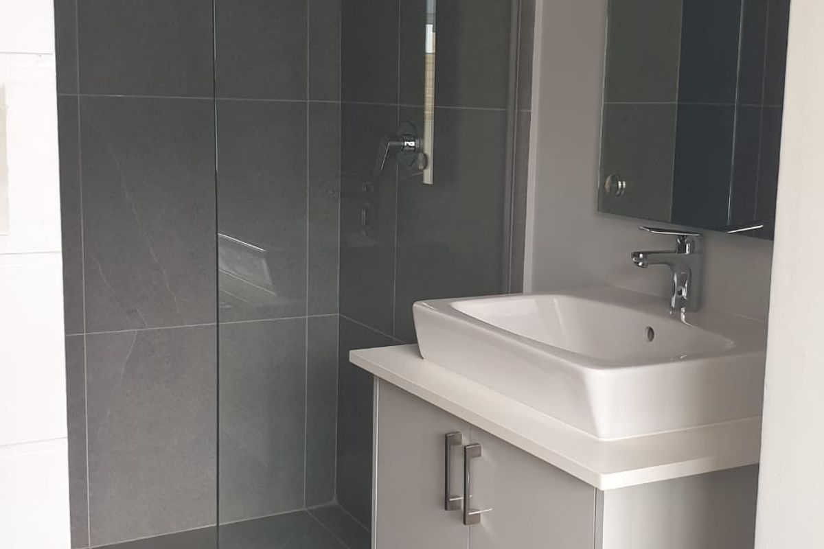 Modern bathroom featuring a wall-mounted vanity with a vessel sink, frameless glass walk-in shower, and contemporary grey tiling.