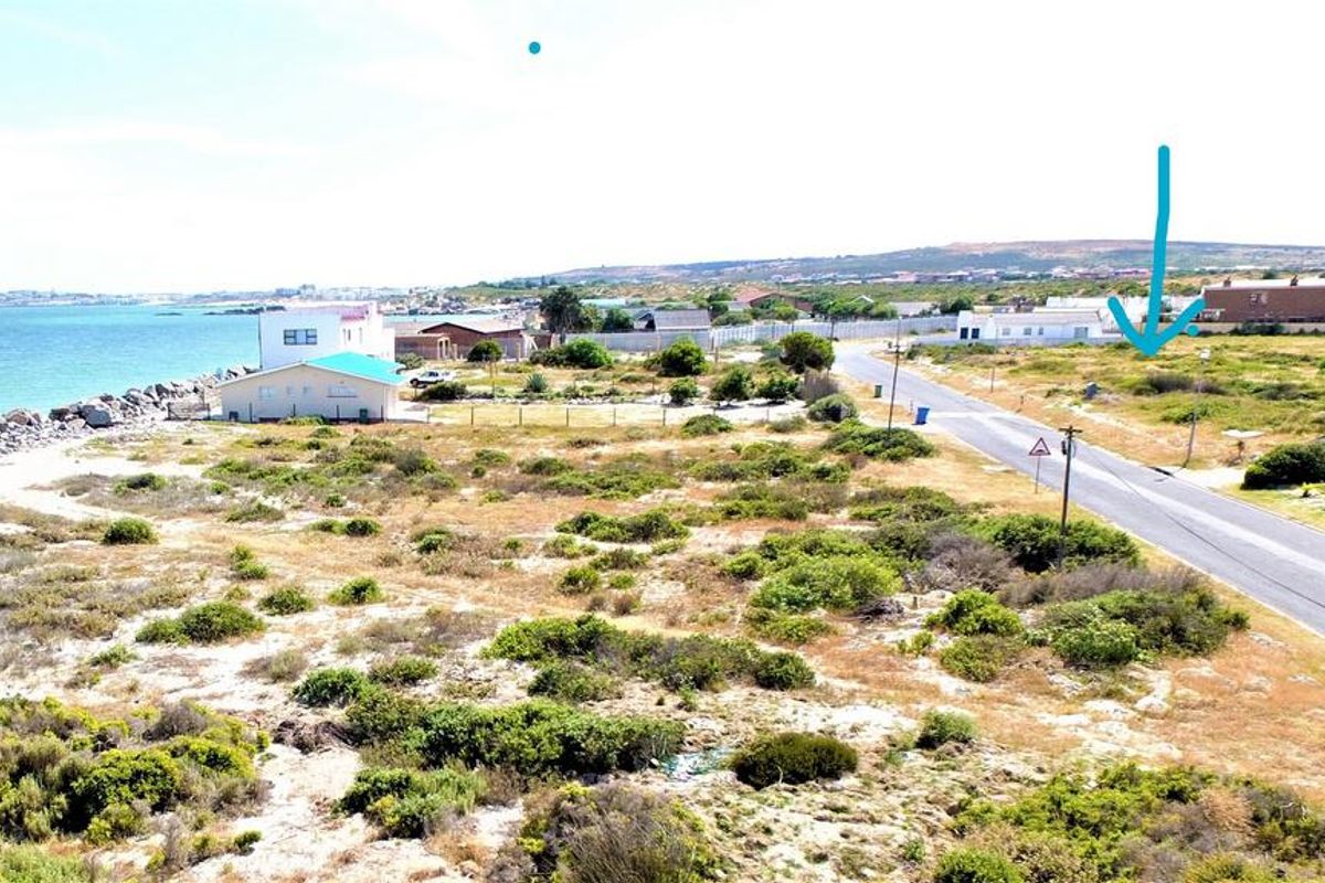 Aerial view of a vacant residential plot situated near the coastline, featuring direct road access and proximity to the ocean.
