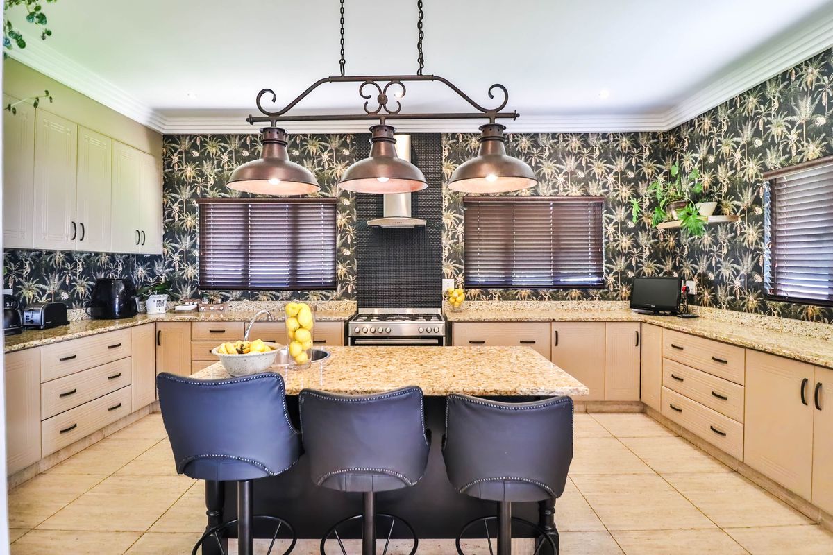 Spacious kitchen featuring granite countertops, a central island, stainless steel gas range with extractor fan, and decorative patterned wallpaper.