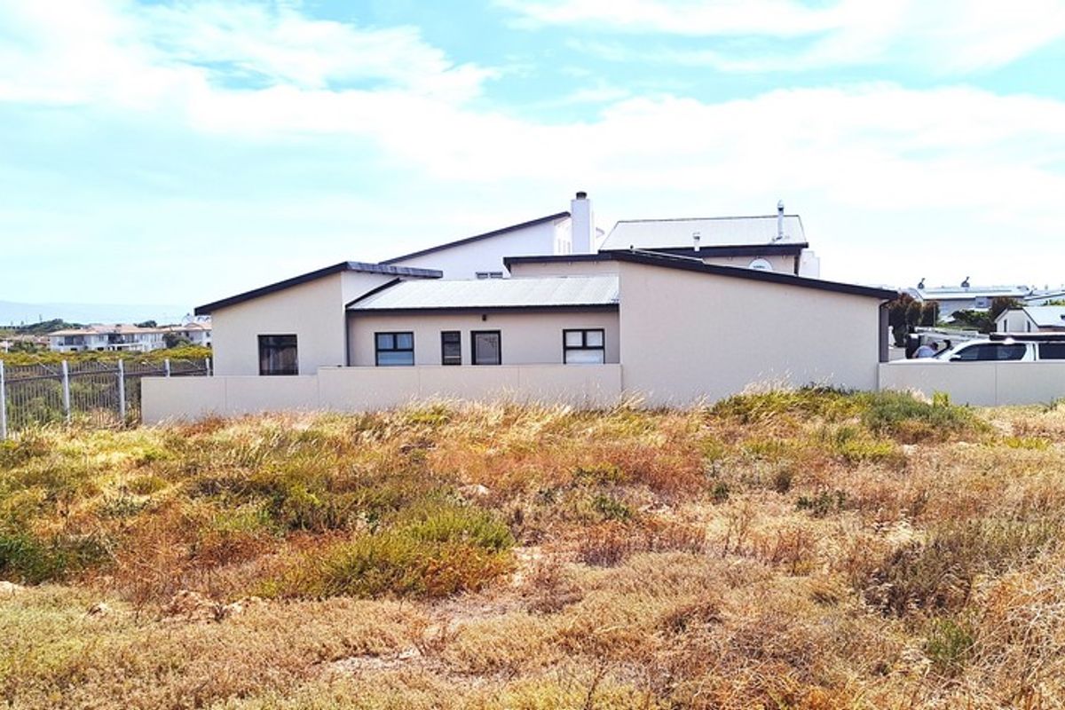 A view of a vacant residential plot featuring natural vegetation, perimeter fencing, and a solar-powered security light, with neighboring properties visible in the background.