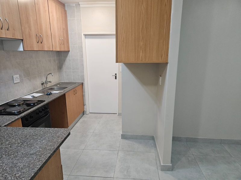 A clean, functional kitchen featuring wood-finish cabinetry, granite countertops, a built-in oven and hob, and neutral tiled flooring.