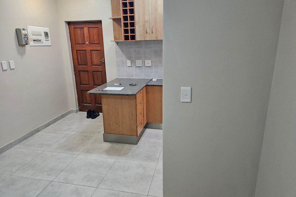 A compact kitchen area featuring light wood cabinetry, granite countertops, a built-in wine rack, and neutral tiled flooring.