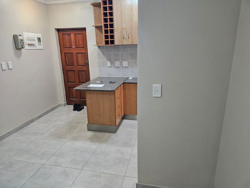 A compact kitchen area featuring light wood cabinetry, granite countertops, a built-in wine rack, and neutral tiled flooring.
