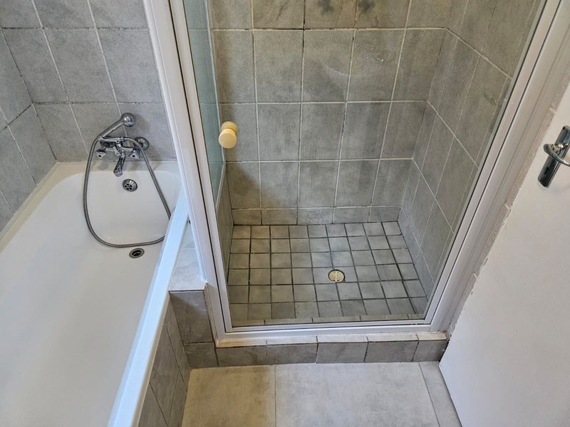 A functional bathroom featuring a separate bathtub and shower enclosure with tiled finishes, requiring cosmetic updates to improve the overall aesthetic.