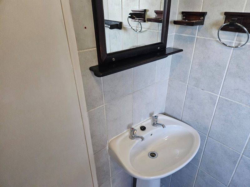 A functional bathroom featuring a white pedestal basin, chrome taps, and wall-mounted mirror with tiled wall finishes.