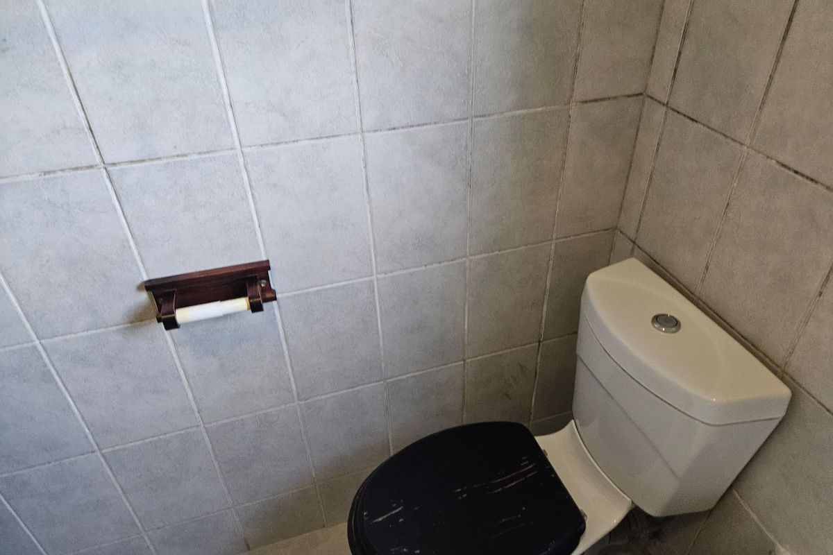 A compact bathroom featuring a standard toilet and tiled walls, showing signs of wear and requiring cosmetic updates.