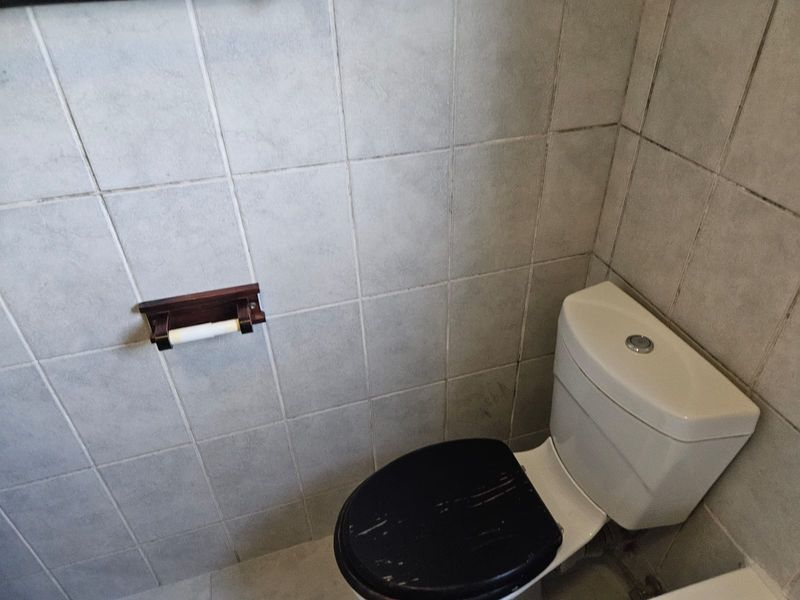 A compact bathroom featuring a standard toilet and tiled walls, showing signs of wear and requiring cosmetic updates.