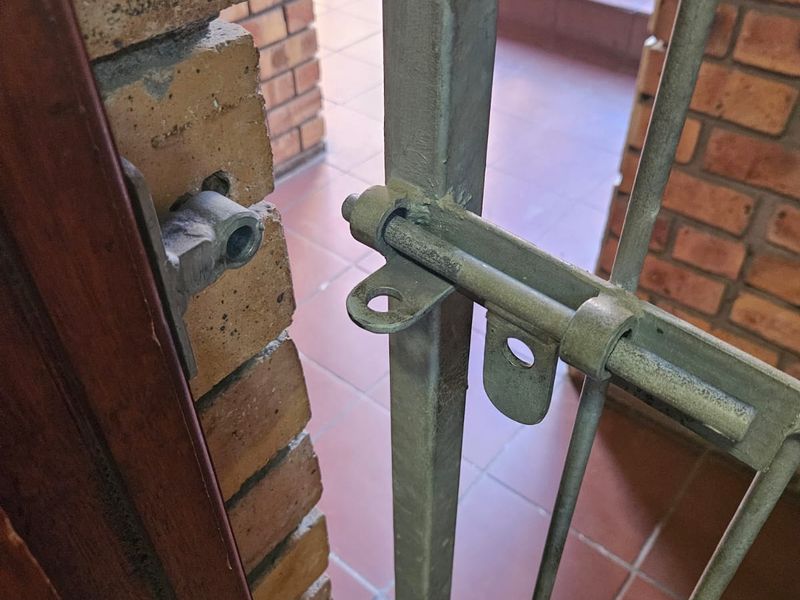 A view of a residential entrance featuring a metal security gate, brick wall construction, and tiled flooring leading to a staircase.