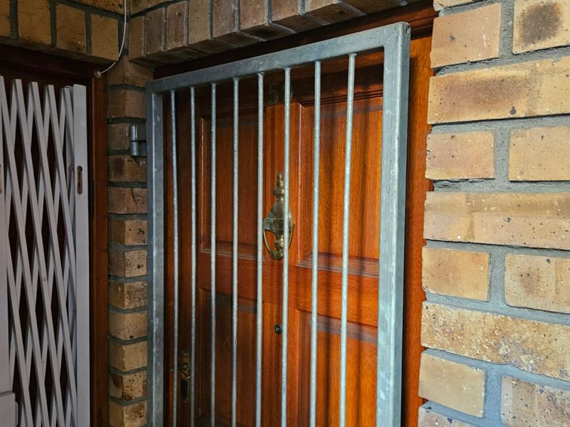 Apartment entrance featuring a solid timber door with a protective metal security gate and classic brick exterior wall finish.