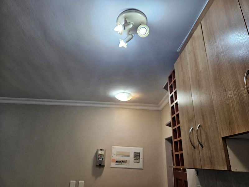 A kitchen area featuring built-in wooden cabinetry, a wine rack, and ceiling-mounted lighting fixtures, with an integrated intercom and electrical distribution board.