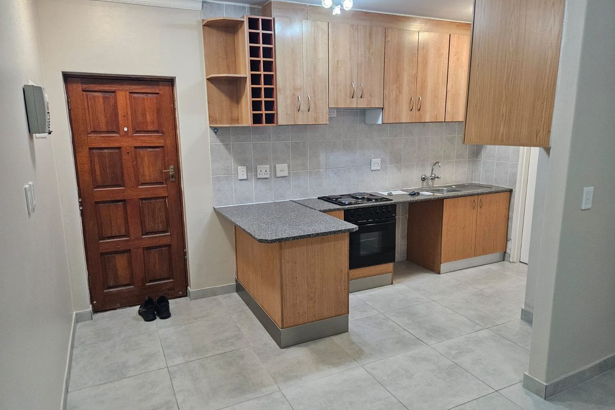A functional kitchen featuring light wood cabinetry, granite-look laminate countertops, built-in oven and hob, and neutral ceramic floor tiling.