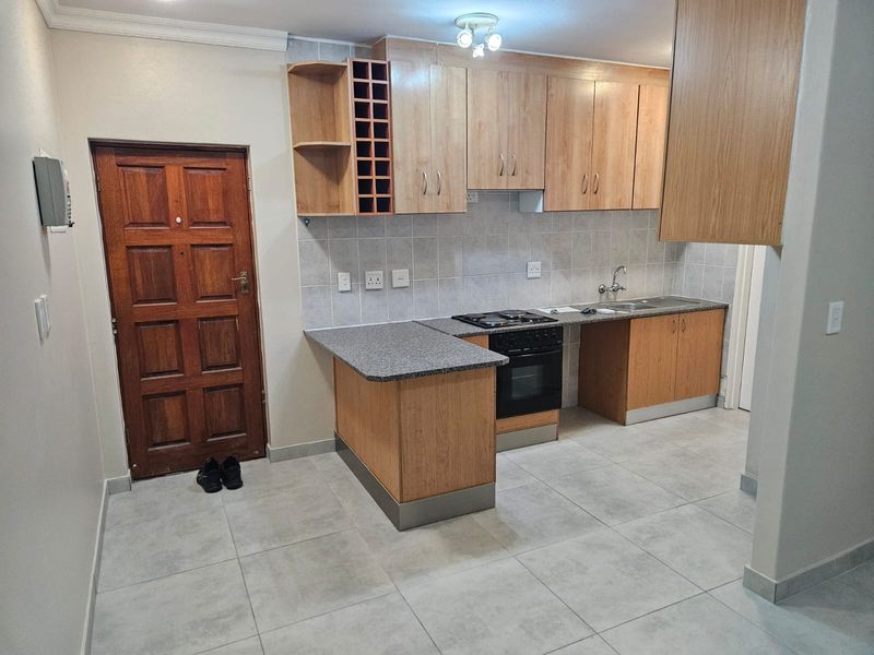 A functional kitchen featuring light wood cabinetry, granite-look laminate countertops, built-in oven and hob, and neutral ceramic floor tiling.