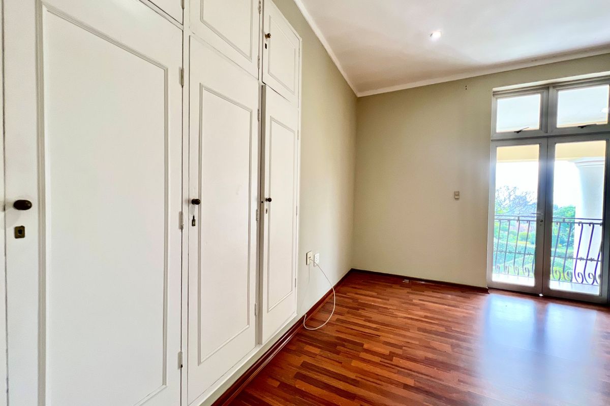 A bright bedroom featuring built-in floor-to-ceiling cabinetry, polished timber flooring, and a glass door providing access to an outdoor balcony.