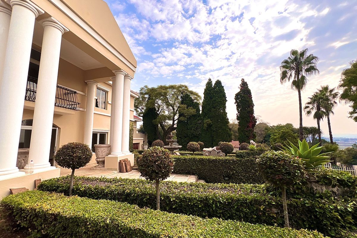 A well-maintained rear garden featuring manicured hedges, topiary trees, and a classic architectural facade with prominent white columns and a balcony.