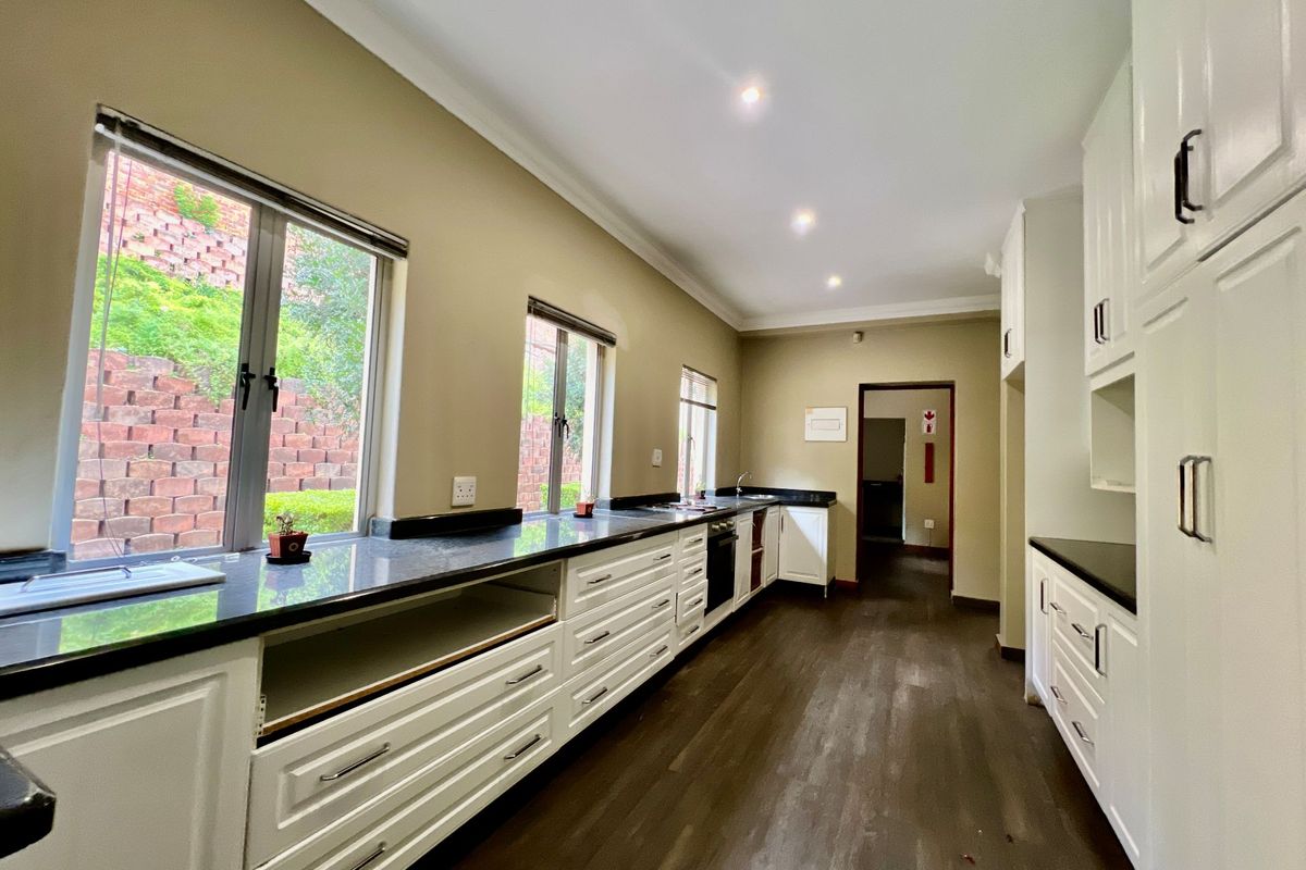 A functional kitchen featuring white cabinetry, dark stone countertops, integrated oven, and large windows overlooking a terraced garden.
