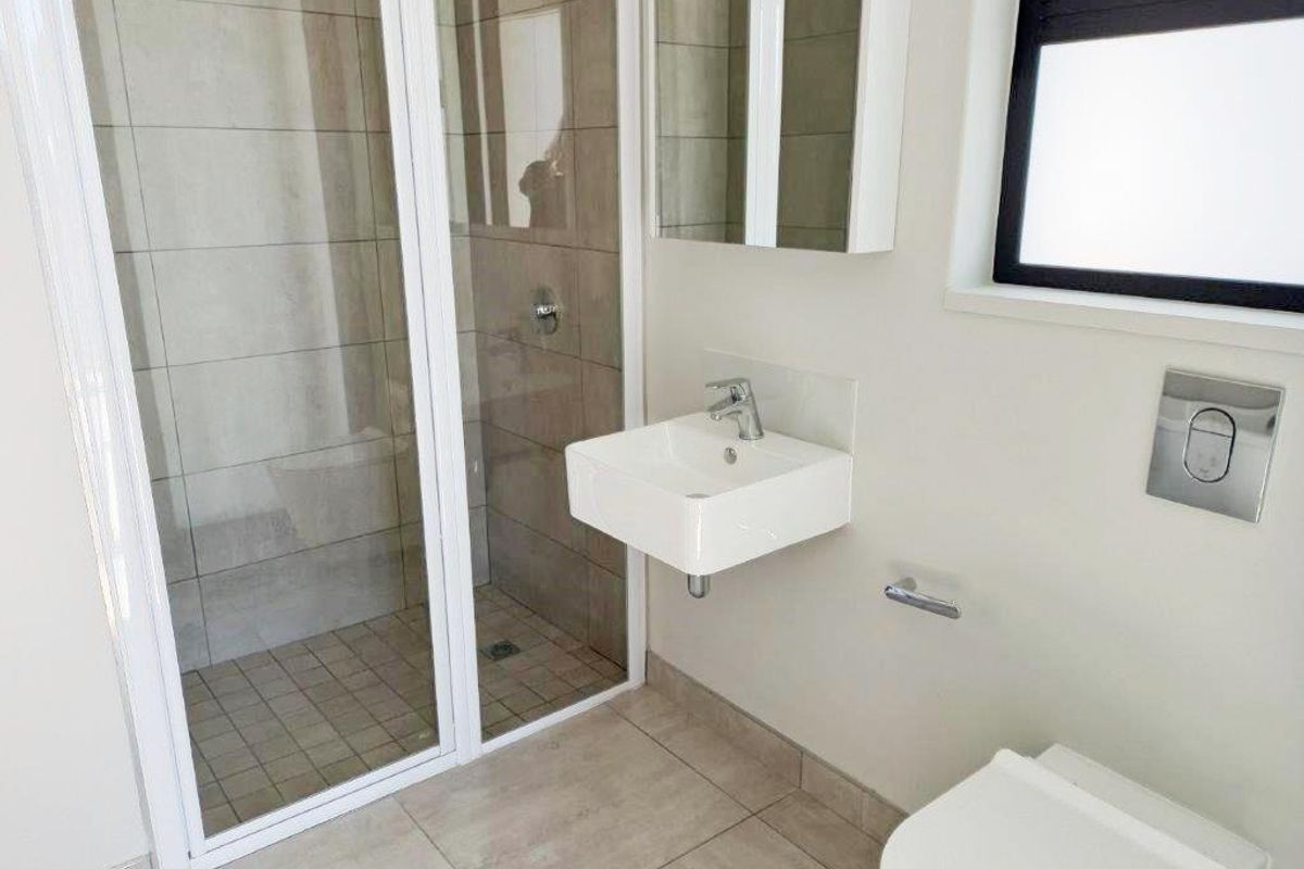 Modern bathroom featuring a glass-enclosed shower, wall-mounted basin, and wall-hung toilet with neutral floor and wall tiling.