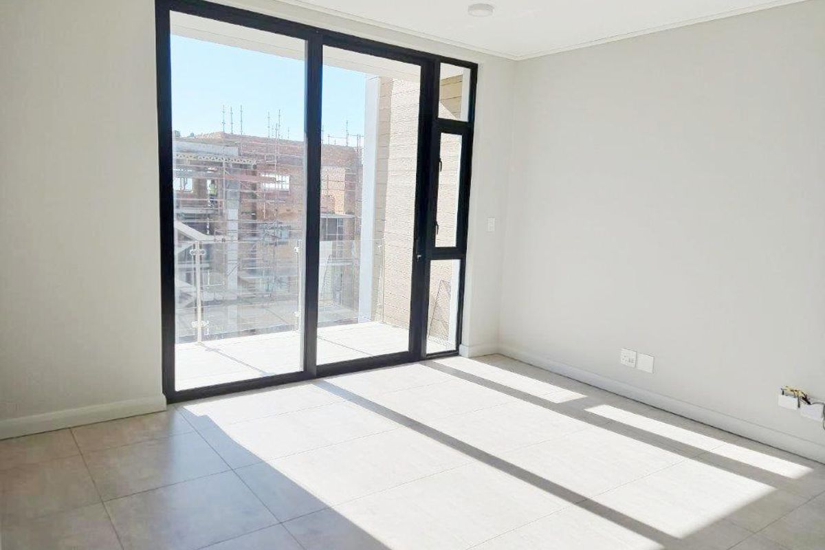 Bright and modern empty living area featuring large sliding glass doors leading to a balcony with neutral tiled flooring throughout.