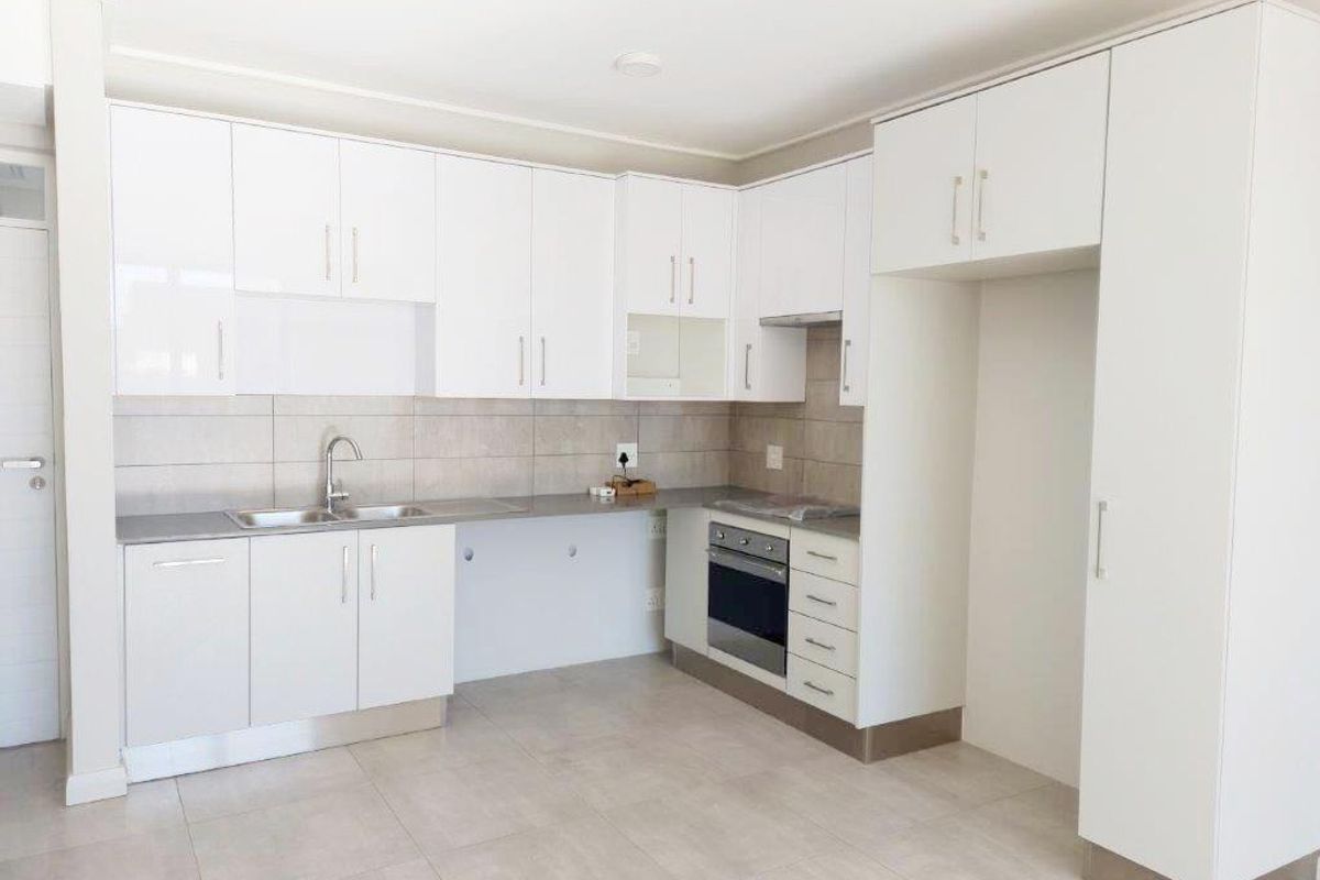 Modern kitchen featuring white built-in cabinetry, tiled backsplash, stainless steel sink, and integrated oven with extractor fan.