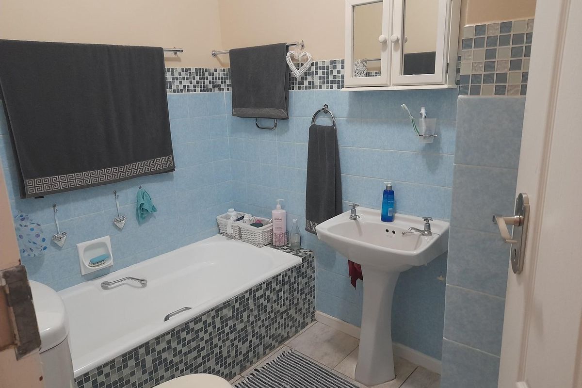 A functional bathroom featuring a bathtub with mosaic tile surround, a pedestal sink, and a wall-mounted medicine cabinet.