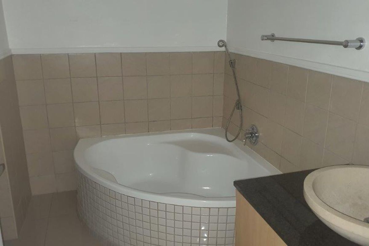 A bathroom featuring a corner bathtub with tiled surround, a vessel sink set into a granite vanity countertop, and a wall-mounted towel rail.